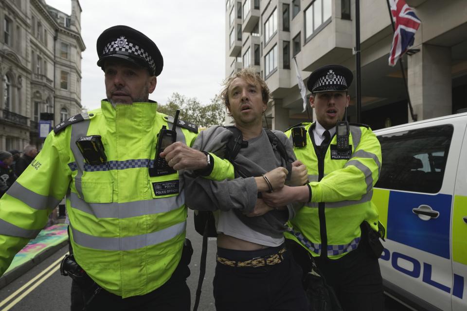 An environmental activists is taken away by police officers outside the Intercontinental Hotel during the Oily Money Out protest, in London, Tuesday, Oct. 17, 2023. (AP Photo/Kin Cheung)