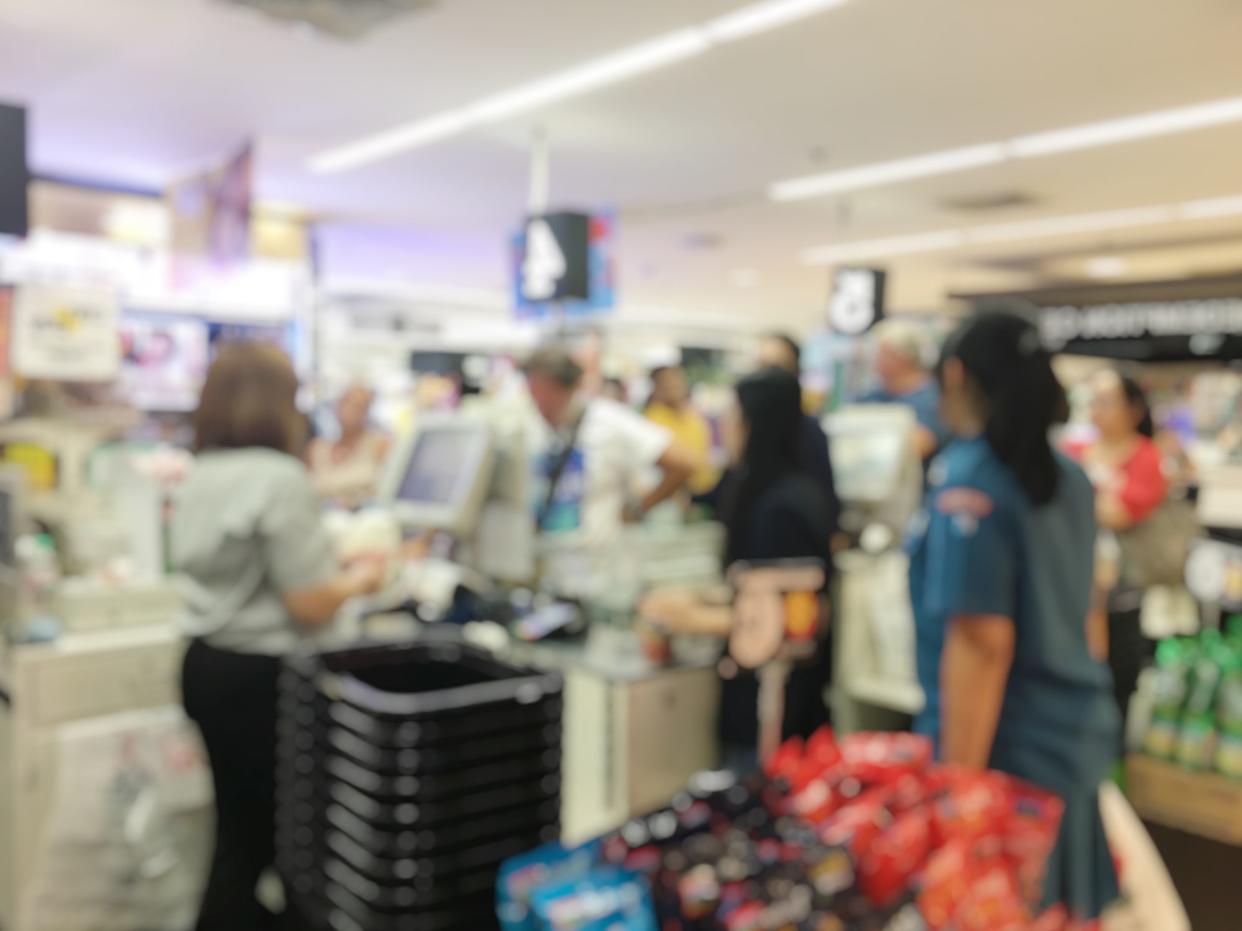 Blurred image of cashier with long line of people at check-out counter of supermarket. Customers paying with credit card or cash to store clerks, full cart of groceries. Cashier register concept