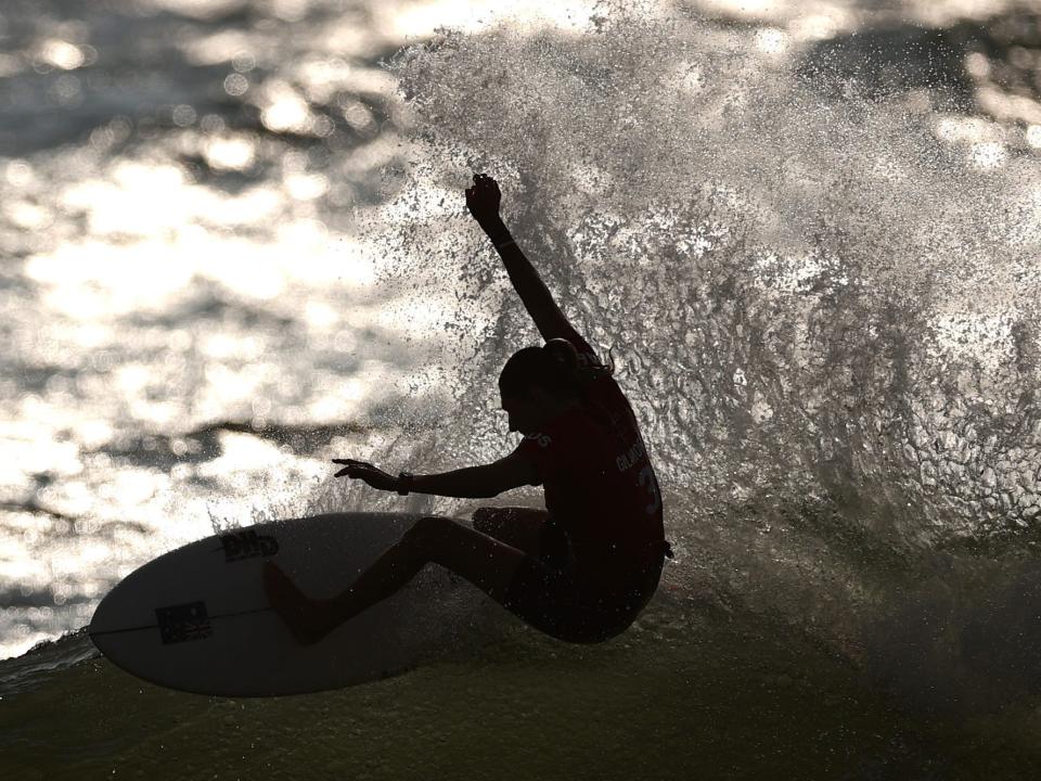 A surfer rides a wave in the sun at the Tokyo Olympics.