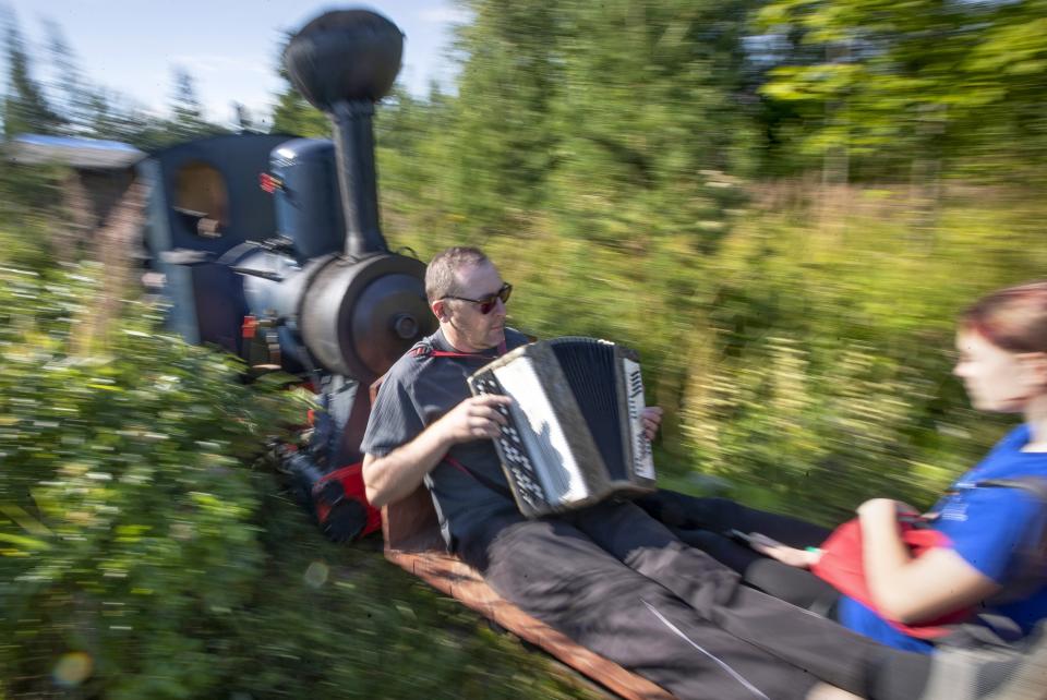 A man plays accordion while riding on Pavel Chilin's miniature steam train in Ulyanovka village outside St. Petersburg, Russia Sunday, July 19, 2020. It took Chilin more than 10 years to build the 350-meter-long miniature personal narrow-gauge railway complete with various branches, dead ends, circuit loops, and even three bridges.(AP Photo/Dmitri Lovetsky)