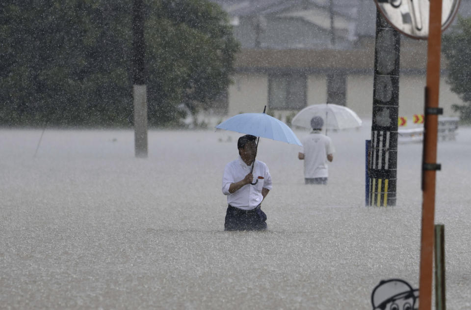 People wade through a street due to a heavy rain in Kurume, Fukuoka prefecture, southern Japan Monday, July 10, 2023. Torrential rain has been pounding southwestern Japan, triggering floods and mudslides. (Kyodo News via AP)