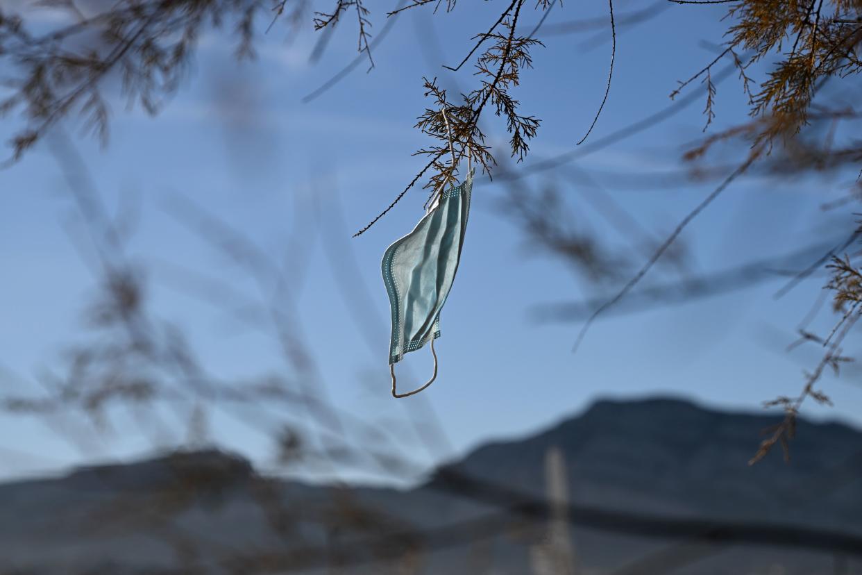 A disposable face mask hangs on a tree. (Photo: NICOLAS TUCAT/AFP via Getty Images)