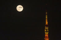 FILE - An airplane flies past the moon rising over Tokyo Tower Saturday, Nov. 20, 2021, in Tokyo. NHK TV said Wednesday, Dec. 1, that Japan will suspend new reservations on all incoming flights for a month to guard against new virus variant. (AP Photo/Kiichiro Sato, File)