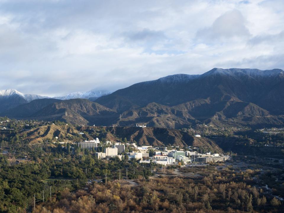 aerial view of nasa jet propulsion laboratory a cluster of buildings in a forested valley below snowy hills