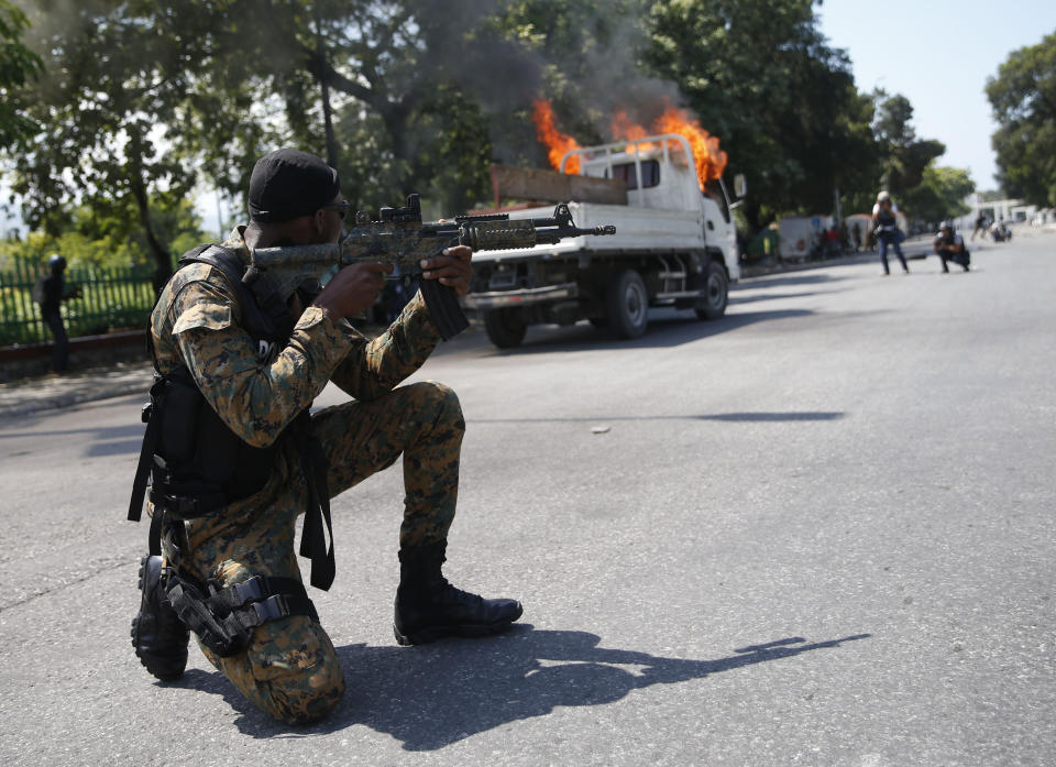 A Presidential Guard point his weapons while taking a position next to his unit's burning truck during clashes with mourners and demonstrators who were carrying the coffins with the remains of two victims of the ongoing violence, near the Presidential Palace in Port-au-Prince, Haiti, Wednesday, Oct. 16, 2019. At last two people were injured in the clashes the while thousands across Haiti attended funerals for protesters who have died in ongoing demonstrations aimed at ousting President Jovenel Moise. (AP Photo/Rebecca Blackwell)