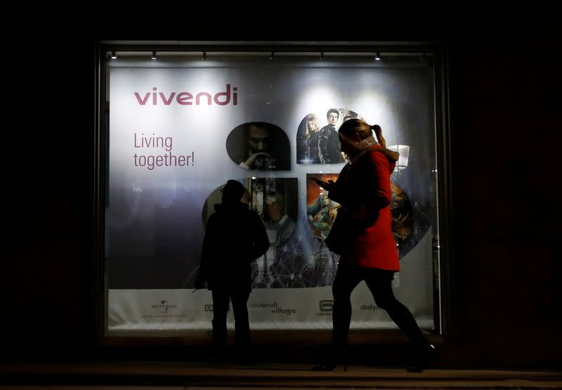 FILE PHOTO: A man stands as a woman walks past a sign of Vivendi at the main entrance of the entertainment-to-telecoms conglomerate headquarters in Paris