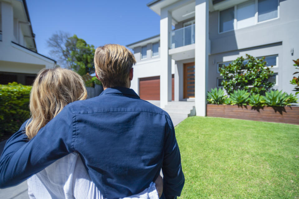 Couple standing in front of their new home. (Source: Getty)