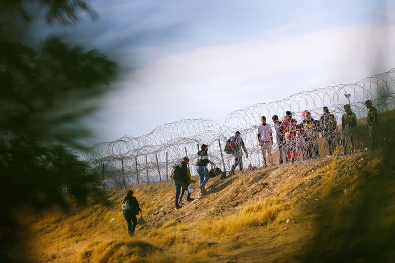 Migrants stand near the border wall, as seen from Ciudad Juarez