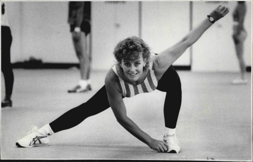 Woman in athletic wear stretches with a smile at a fitness class in Rewind-themed article