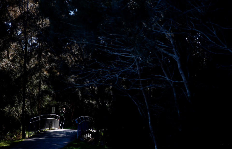 Sam Ware, 22, steps into a ray of sunlight while walking through a park in The Entrance, Central Coast, Australia, Thursday, July 25, 2019. His mother, Deb, watched the kind-hearted, funny boy she loved rapidly disappear as his opioid addiction took hold. In his place was a deceptive, desperate stranger whose soul seemed to have been sucked from his body. Looking back now, she marvels at how fast it all happened. "You become the drug," she says. "It's only a matter of five days before Sam was gone." (AP Photo/David Goldman)