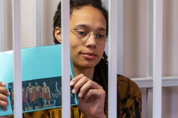 PHOTO: WNBA star and two-time Olympic gold medalist Brittney Griner holds up a photo of players from the all star game wearing her number, while sitting in a cage in court prior to a hearing, just outside Moscow, July 15, 2022. (Dmitry Serebryakov/AP)