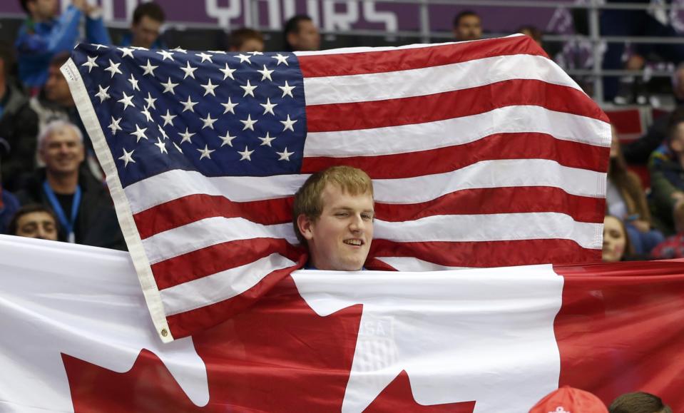Fans raise U.S. and Canadian flags as they watch the men's preliminary round ice hockey game between Canada and Norway at the Sochi 2014 Sochi Winter Olympics, February 13, 2014. REUTERS/Gary Hershorn (RUSSIA - Tags: OLYMPICS SPORT ICE HOCKEY)