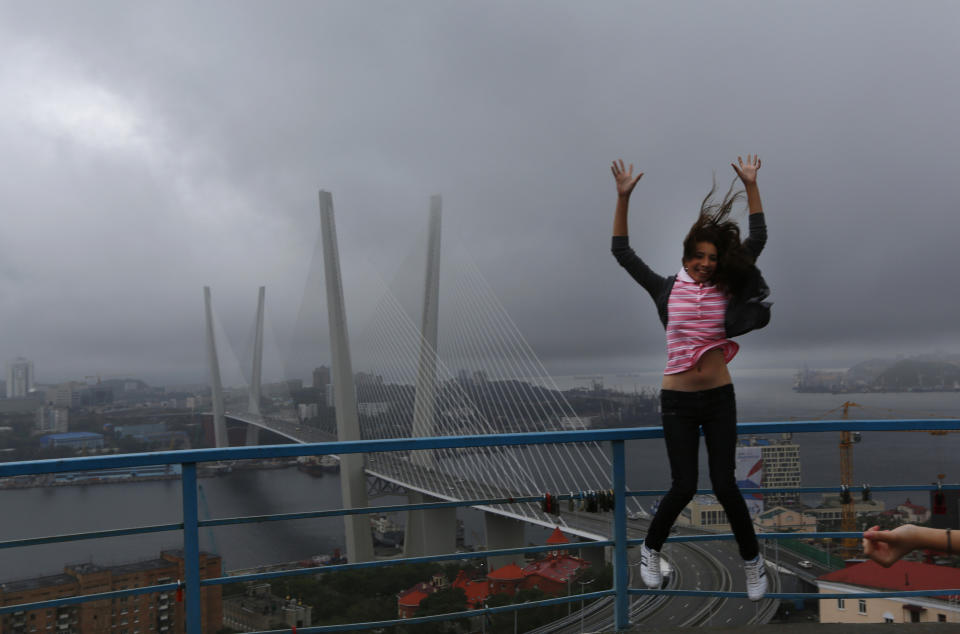 A woman jumps as she poses for a picture in front of a cable-braced bridge in the eastern Russian city of Vladivostok Wednesday, Sept. 5, 2012. Once a mysterious closed city during Soviet times, Vladivostok is ready to strut in the world spotlight as host of the Asia-Pacific Economic Cooperation summit. Russia has splashed $20 billion preparing for the summit in Vladivostok, its largest but long-neglected Pacific port, as part of a grand plan to become a bigger player on Asian markets. (AP Photo/Vincent Yu)