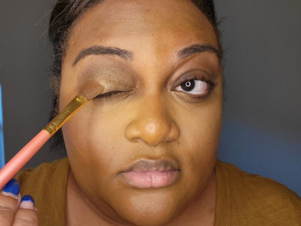 The writer applies a shimmery brown eyeshadow color to her lid with a brush