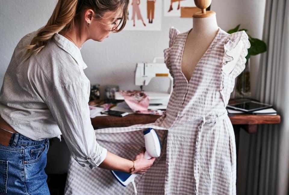 A woman steams a dress on a mannequin.