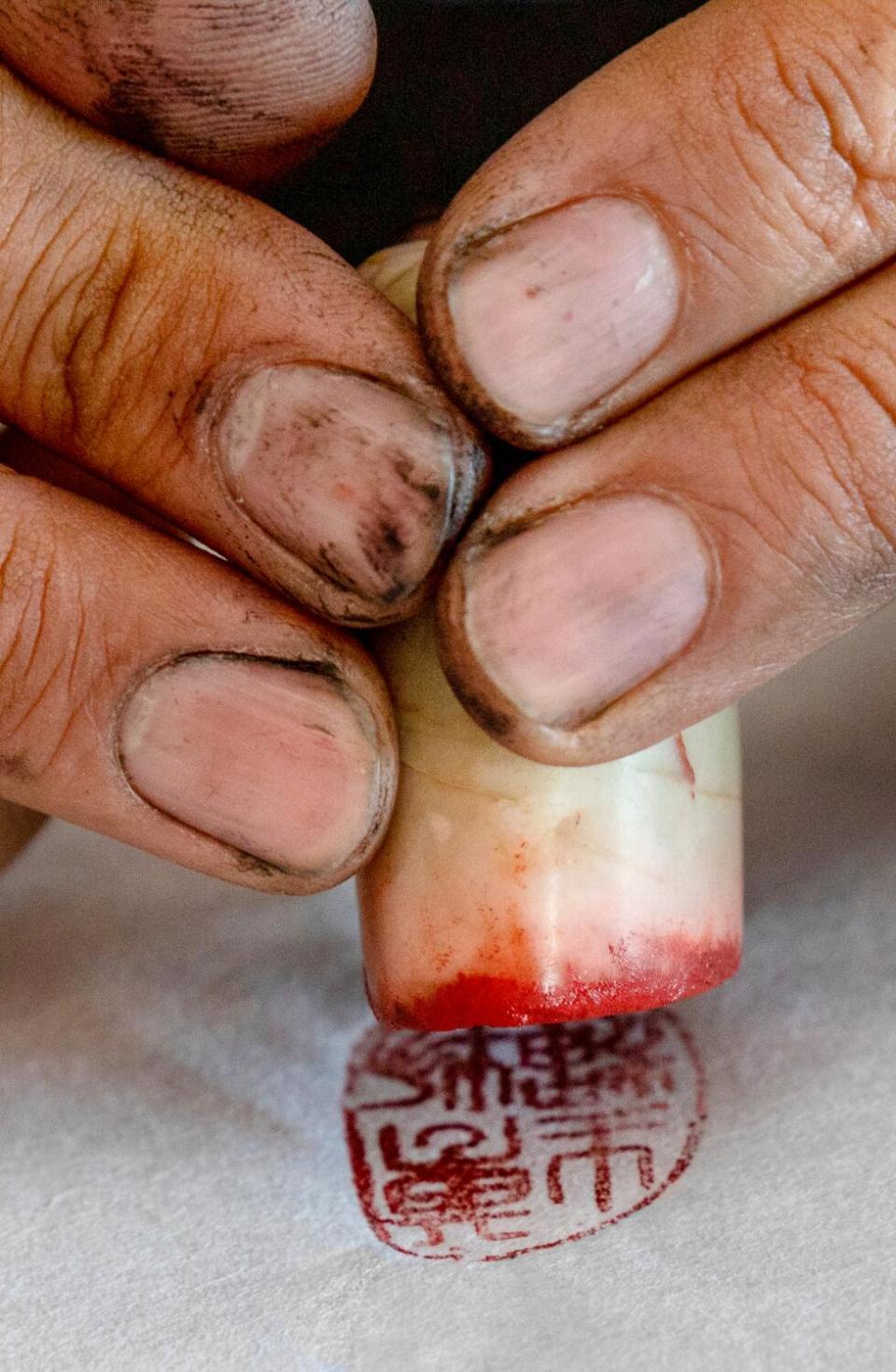 A detail photo of an artist's ink-stained fingers stamping a gyotaku.