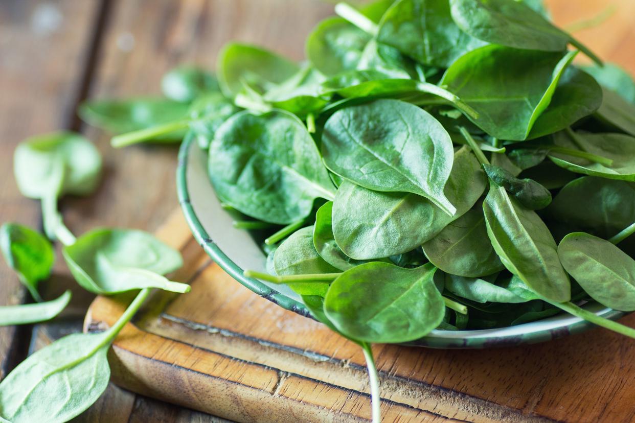 Closeup of spinach leaves in a ceramic bowl on a wooden cutting board, selective focus, surrounded by spinach leaves, on a wooden table, blurred