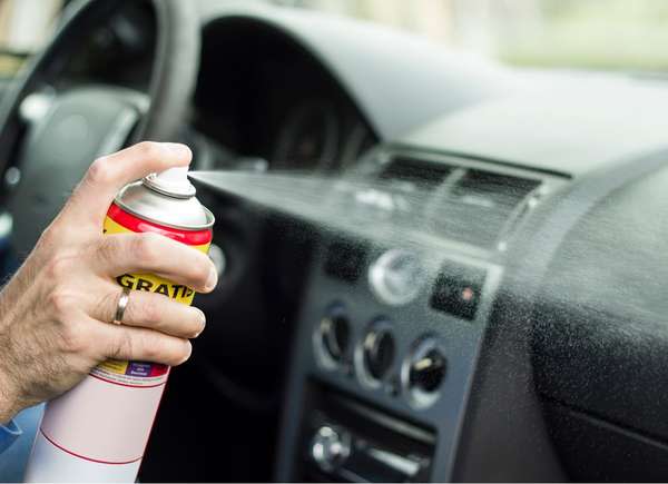 Person using an aerosol spray cleaner on car interior and dashboard.