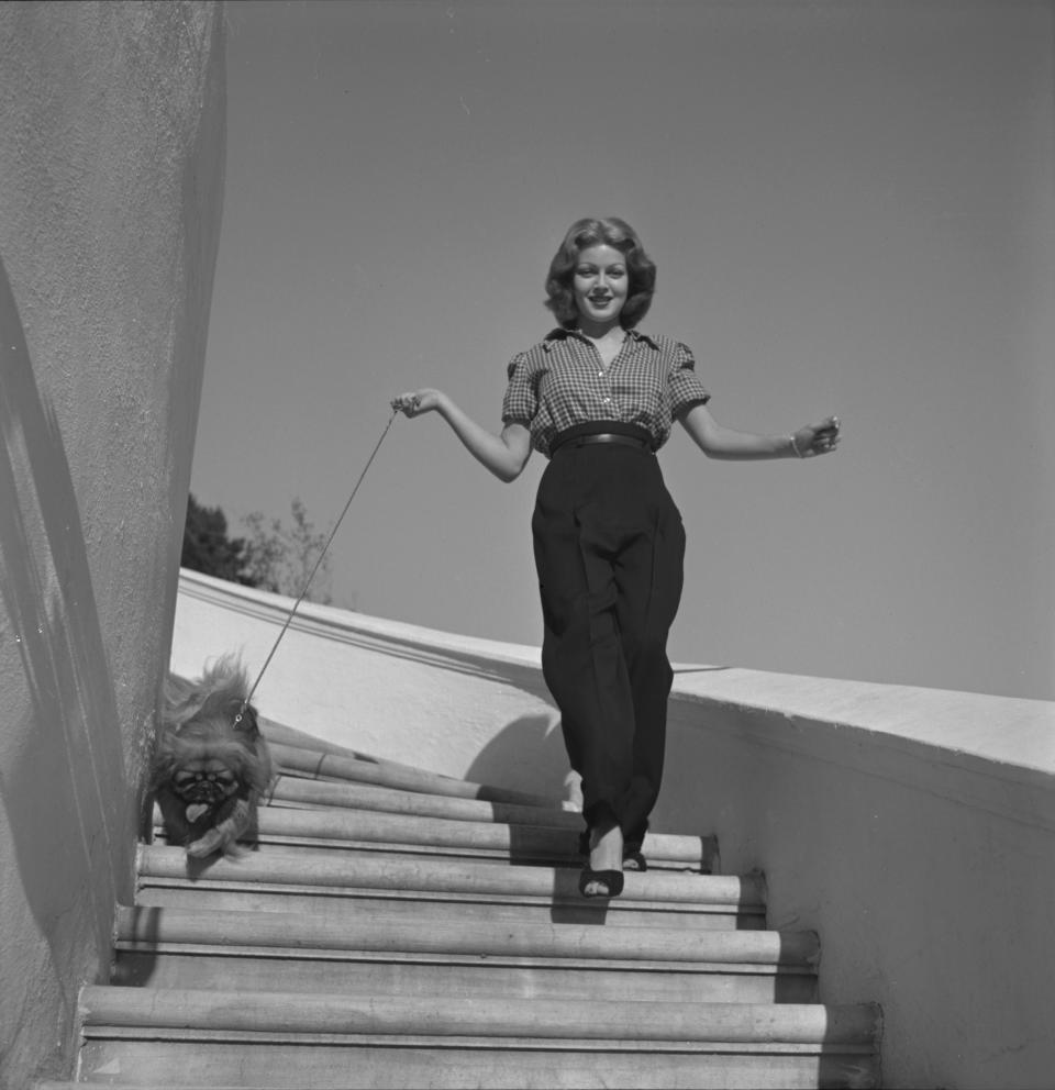 Lana Turner walks down a staircase with her Pekingese dog in Hollywood, California, 1940.