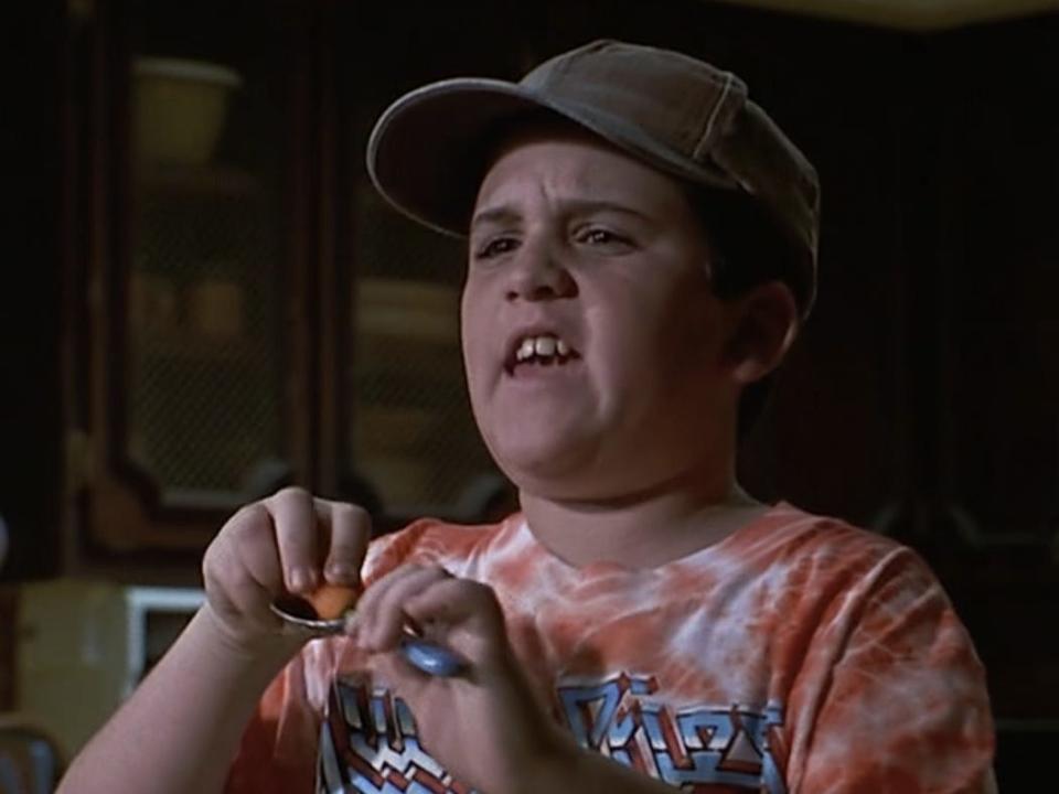 Brian Levinson as Michael in a kitchen wearing a tan baseball cap and an orange tie-dye shirt and holding a spoon with a carrot on it