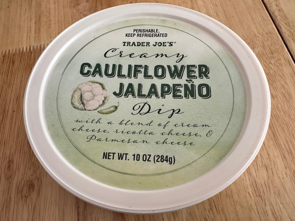 Green and white tub of Trader Joe's cauliflower and jalapeno dip on wood table