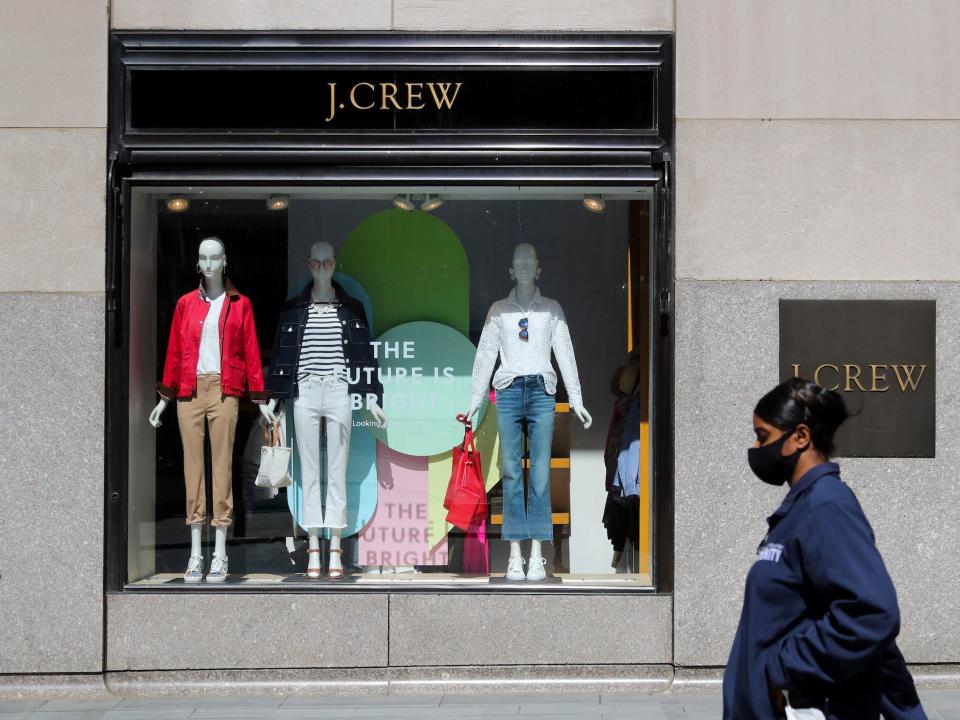 Woman wearing mask walks past J. Crew store that's window says "the future is bright"