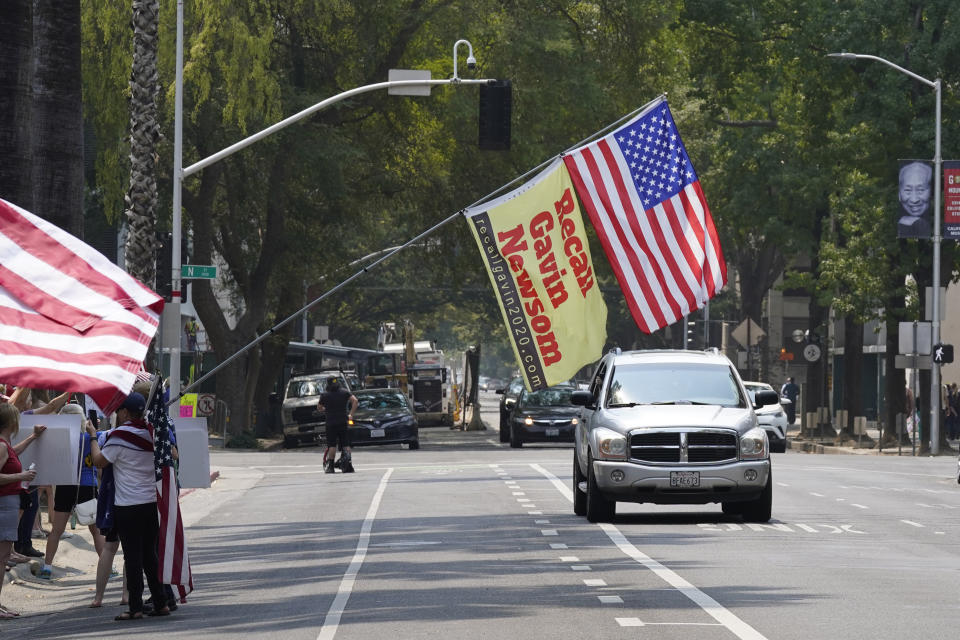 A flag calling for the recall of Gov. Gavin Newsom hangs in front of cars passing the Capitol during a demonstration against mandatory vaccinations in Sacramento, Calif., Monday, Aug. 16, 2021. California is mandating COVID-19 vaccinations for all health care workers and will require state government and school staff to be vaccinated or regularly tested. (AP Photo/Rich Pedroncelli)