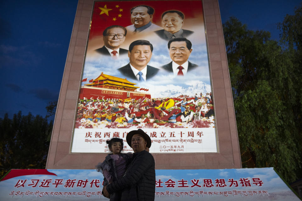 FILE - A man holds a girl as they pose for a photo in front of a large mural depicting Chinese President Xi Jinping, bottom center, and other Chinese leaders at a public square at the base of the Potala Palace in Lhasa in western China's Tibet Autonomous Region on June 1, 2021. An extensive report by Human Rights Watch says China is accelerating the forced urbanization of Tibetan villagers and herders, adding to state government and independent reports of efforts to assimilate them through control over their language and traditional Buddhist culture. (AP Photo/Mark Schiefelbein, File)