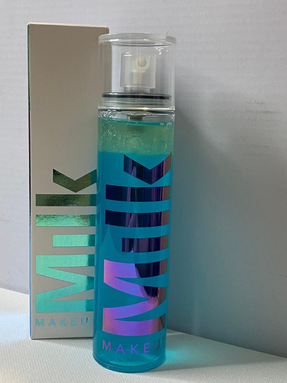 A blue spray bottle of with iridescent &quot;Milk&quot; text on side with a box with similar iridescent text to left of spray