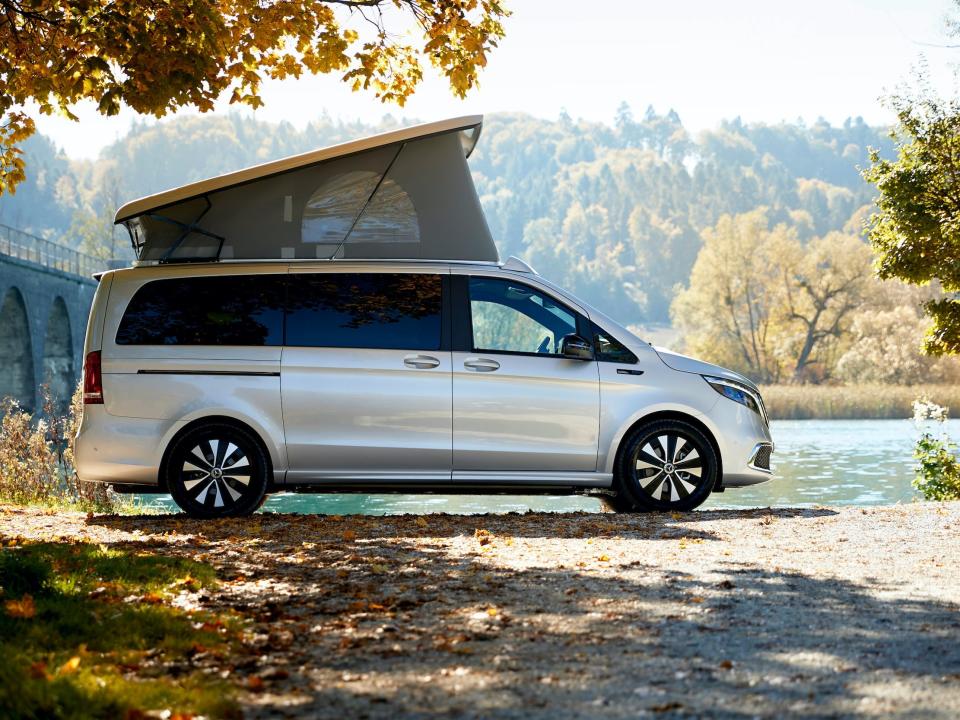 The Mercedes-Benz EQV with a pop-top roof next to a body of water surrounded by trees, nature.