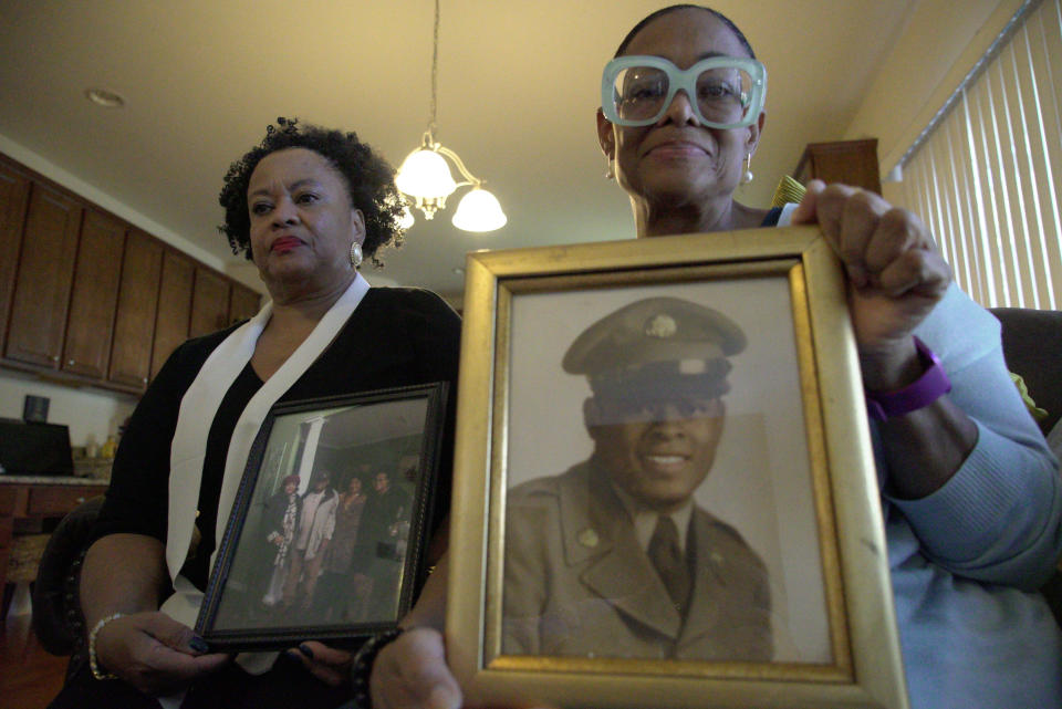 Sisters Barbara Leak-Watkins, right, and Alberta Lynn Fantroy pose with photos of their late father, Alex Leak Jr., at Watkins' home in Greensboro, N.C., on Wednesday, Nov. 4, 2020. The Army veteran died in July after collapsing from dehydration at his assisted-living facility, and the family believes pandemic-related neglect is to blame. As more than 90,000 of America’s long-term care residents have died in a coronavirus pandemic that has pushed staffs to the limit, advocates for the elderly say a tandem wave of death separate from the virus has quietly claimed thousands more, often because overburdened workers haven’t been able to give them the care they need. (AP Photo/Allen G. Breed)