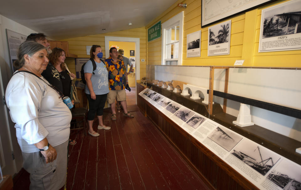 In this Monday, Jan. 10, 2022, photo provided by the Florida Keys News Bureau, Celeste Trzcinski, a tour guide at Pigeon Key, shows visitors a portion of a museum that chronicles the building of the Old Seven Mile Bridge in the Florida Keys. The historic bridge to Pigeon Key has undergone a 4.25-year, $44 million restoration effort and is to reopen Wednesday, Jan. 12, 2022, to pedestrians, bicyclists, anglers and visitors to Pigeon Key. The old bridge originally was part of Henry Flagler's Florida Keys Over-Sea Railroad that was completed in 1912. The railroad ceased operations in 1935 and was converted into a highway that opened in 1938. In 1982, construction was completed on a new Seven Mile Bridge that continues to carry motor vehicles between the South Florida mainland throughout the Keys to Key West. (Andy Newman/Florida Keys News Bureau via AP)