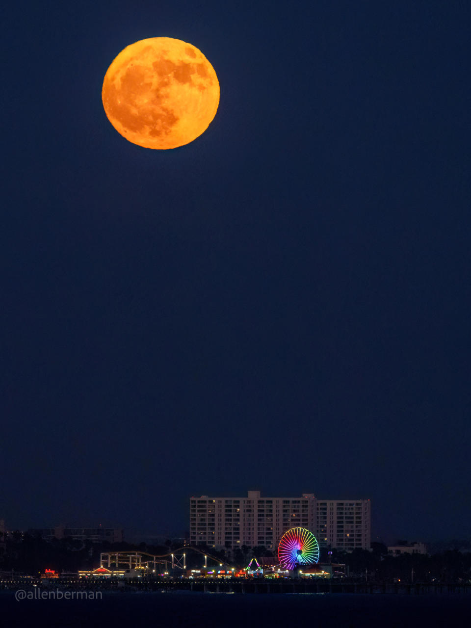 full moon shining in sky above skyline and colorful ferris wheel