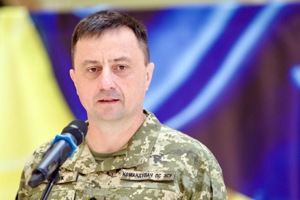 Mykola Oleschuk standing in front of a microphone against a blue and yellow background.