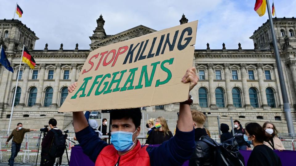 Man holds sign reading, "Stop killing Afghans," in front of the German parliament building