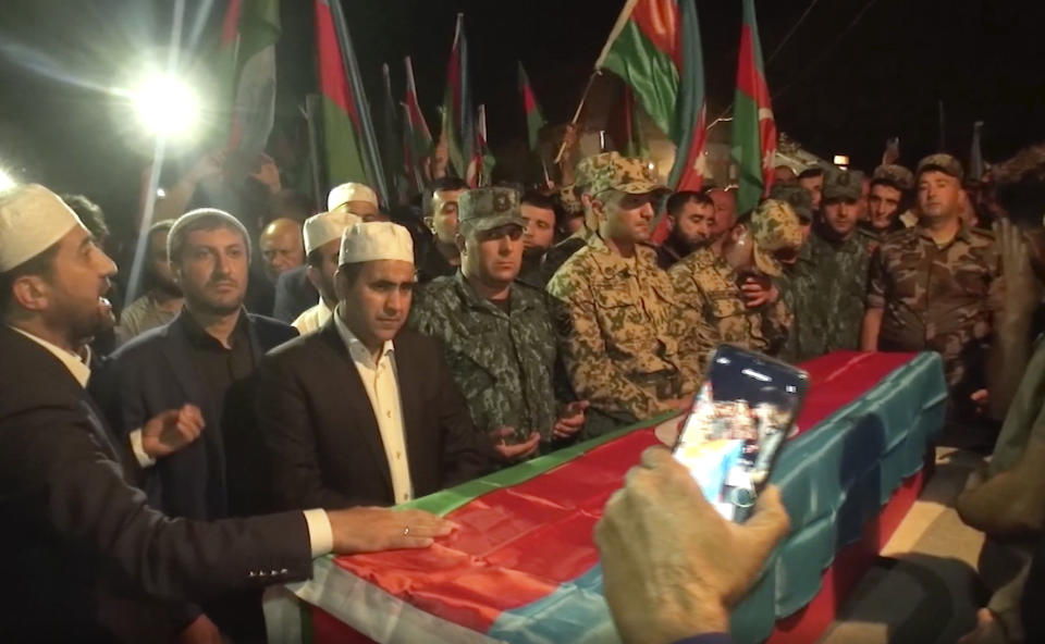 In this image taken from video, people stand around a coffin of Azeri serviceman Elshan Babazade killed at Azerbaijani-Armenian border, during his funeral in Mykhlygovag, Azerbaijan, Tuesday, Sept. 13, 2022. Armenia and Azerbaijan accused each other of new rounds of shelling on Wednesday morning as hostilities reignited between the two longtime adversaries. (AP Photo)