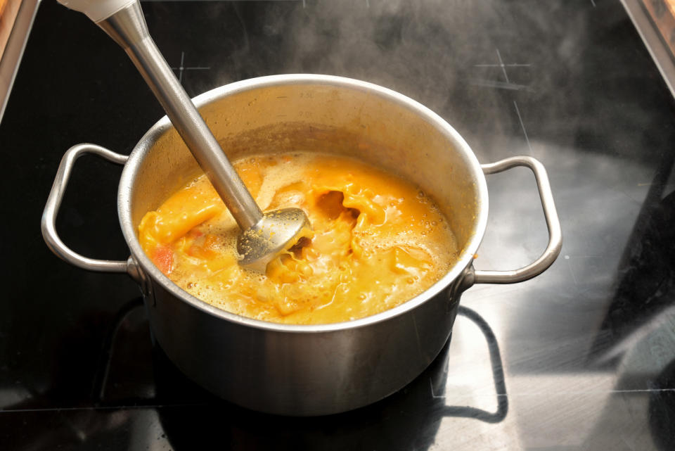 An immersion blender in a pot of soup.