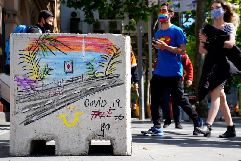 People in face masks walk past a 'COVID-19 Free' sign after coronavirus disease restrictions were eased in Melbourne