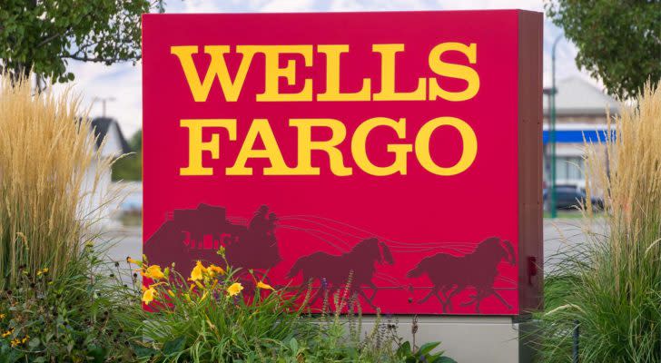 Wells Fargo (WFC) bank sign in yellow and red with wagon logo. The sign is flanked by tall grass