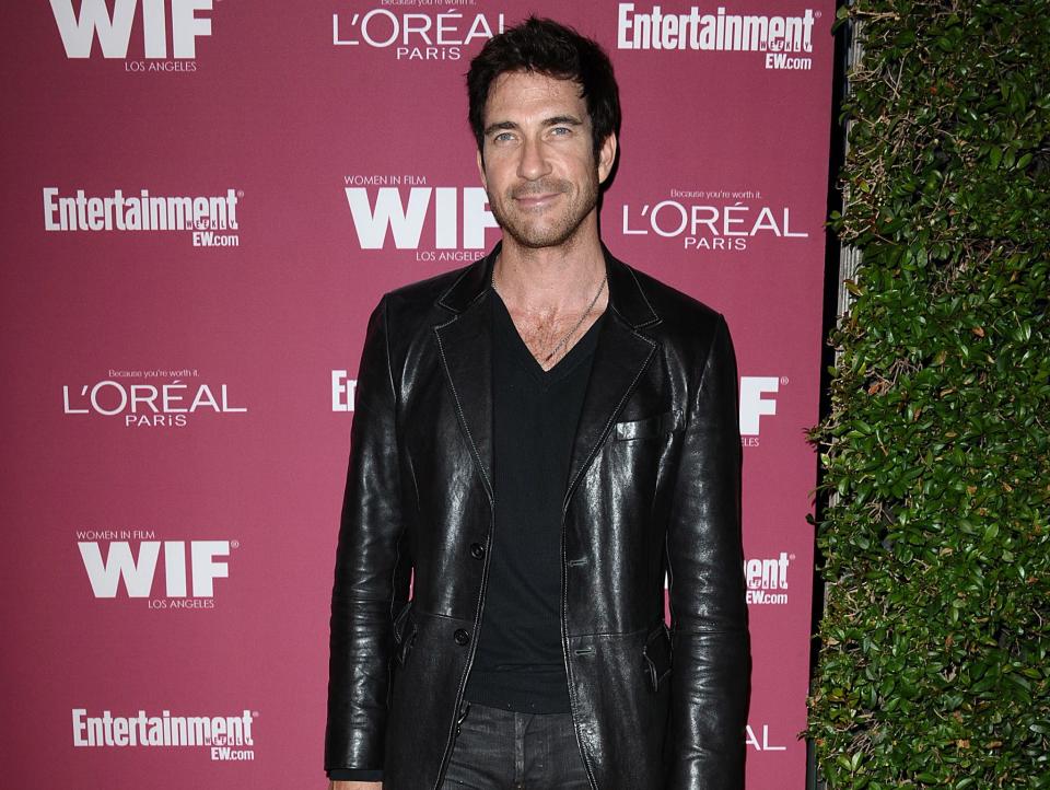 Dylan McDermott in 2011 wearing a red jacket in front of pink wall