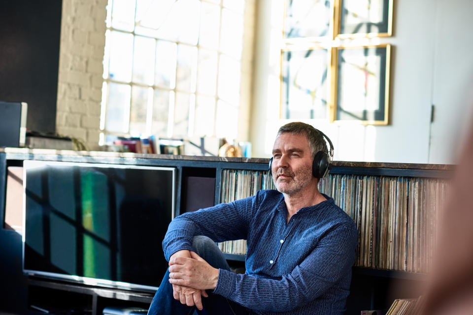 Man sitting by record collection listening to music on headphones, thoughtful, memories, relaxing