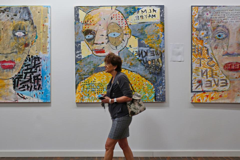 A woman walks past paintings by Patrick Moore during an announcement of a dynamic new funding and support program for local artists at an event held at the Hatch Street Studios in New Bedford.