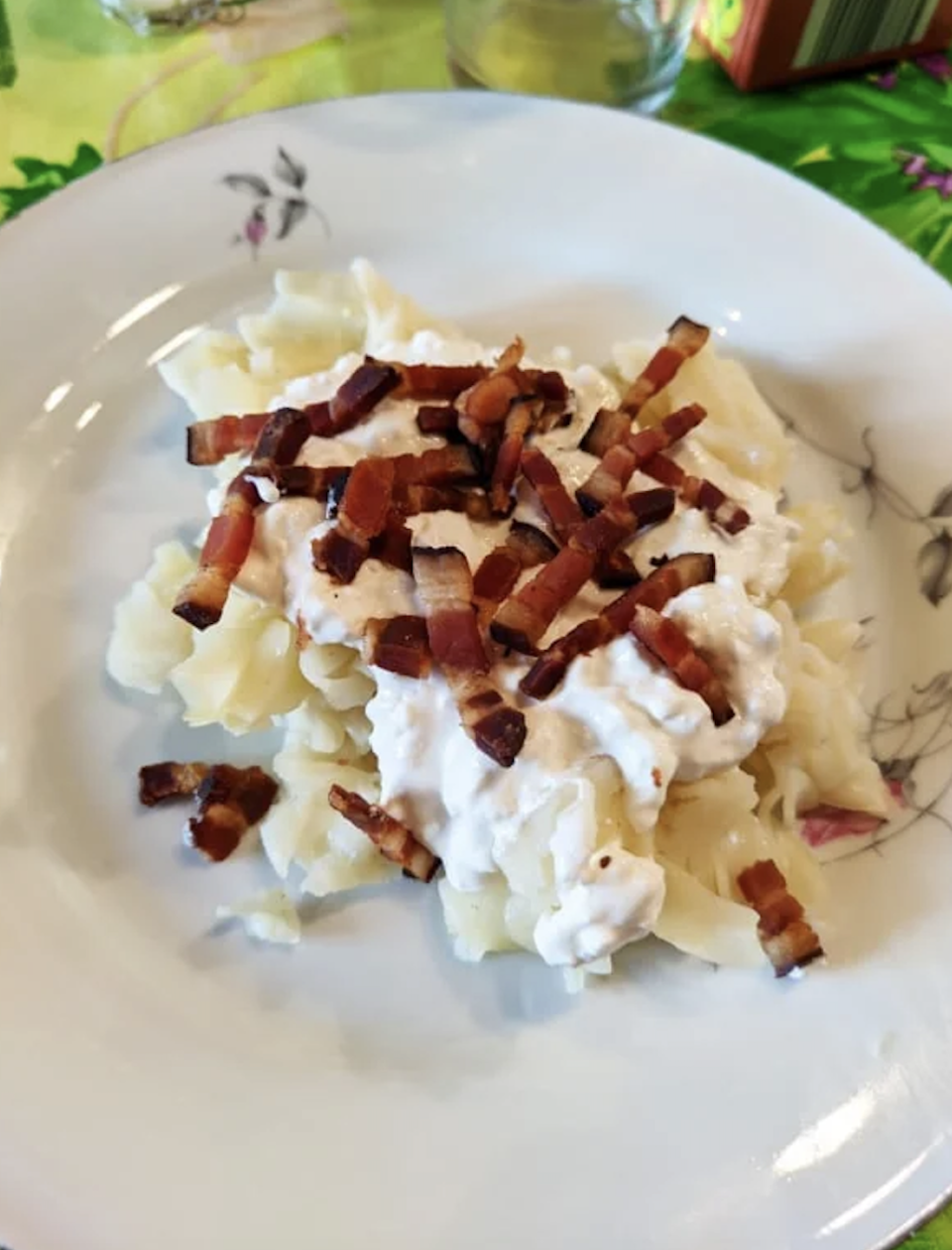 A plate of dumplings topped with a creamy sauce and diced crispy bacon. The dish is served on a white plate with a floral pattern