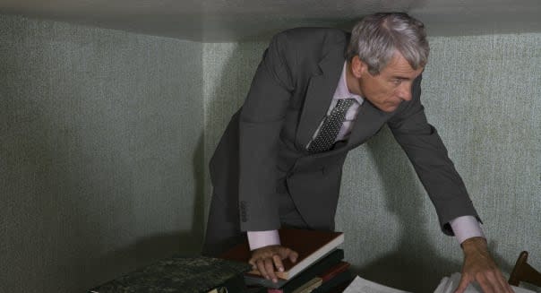 Mature businessman standing at desk stooping under low ceiling