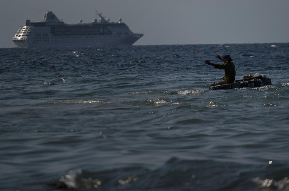 A man fishes in the sea on a makeshift raft while the Empress of the Seas, a Royal Caribbean vessel, leaves the harbor in Havana, Cuba, Wednesday, June 5, 2019. Major cruise lines on Wednesday immediately began dropping stops in Cuba from their itineraries and hastily rerouting ships to other destinations including Mexico, after the Trump administration's new restrictions on travel to Cuba. (AP Photo/Ramon Espinosa)