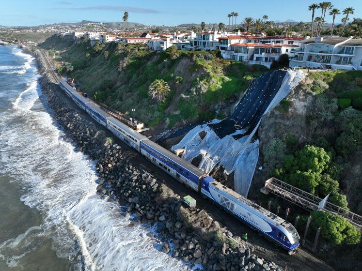 San Clemente, CA - March 08: An aerial view of Amtrak Pacific Surfliner resuming service while passing through the repaired tracks and barrier wall construction at Mariposa Point in San Clemente Friday, March 8, 2024. Rail service is on a limited basis. The reopening of the line this week marked the first time in more than a month that passengers have been able to hop aboard Amtrak's Pacific Surfliner and ride through the coastal swath between Orange County and San Diego. Construction continues on the barrier wall, which will be 10 to 15 feet high and 192 feet long. A series of powerful winter storms saturated the hillside adjacent to the tracks, causing it to slide and crumble, and forcing officials to halt train service for weeks. (Allen J. Schaben / Los Angeles Times)