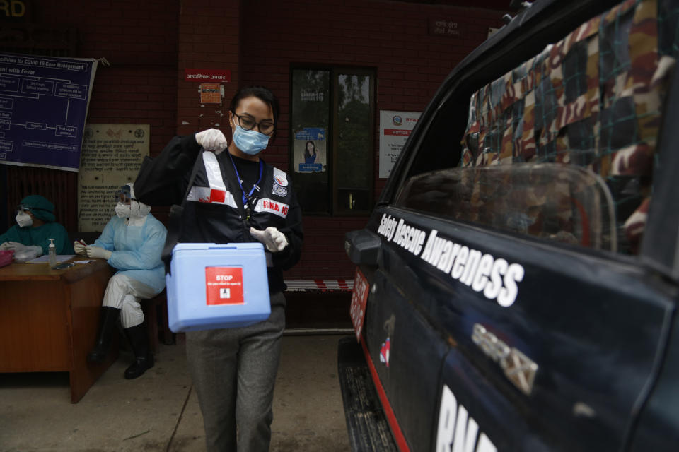 Punam Karmacharya, 22, of the RNA-16 volunteer group, carries a box containing swab samples of patients to deliver it to a testing center, at a hospital in Bhaktapur, Nepal, Tuesday, May 26, 2020. RNA-16 stands for “Rescue and Awareness” and the 16 kinds of disasters they have prepared to deal with, from Nepal’s devastating 2015 earthquake to road accidents. But the unique services of this group of three men and a woman in signature blue vests in the epidemic amount to a much greater sacrifice, said doctors, hospital officials and civic leaders. (AP Photo/Niranjan Shrestha)
