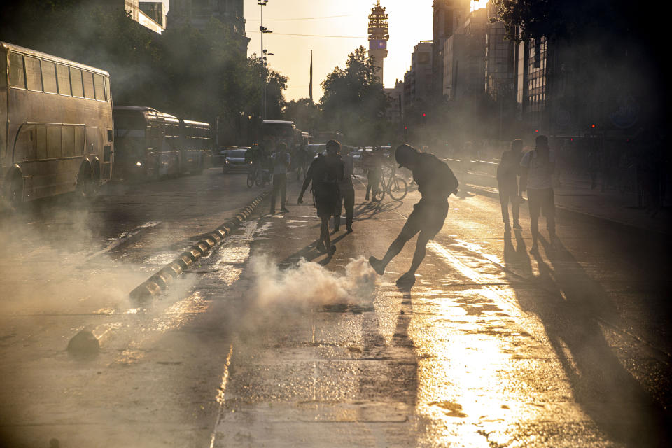 A protester kicks a tear gas canister launched by police near to the Santa Lucia subway station during a protest against the rising cost of subway and bus fares, in Santiago, Friday, Oct. 18, 2019. (AP Photo/Esteban Felix)