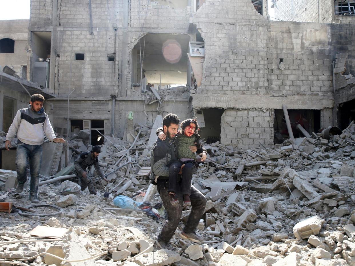 A man carries an injured boy as he walks on rubble of damaged buildings in the rebel held besieged town of Hamouriyeh, eastern Ghouta: Reuters