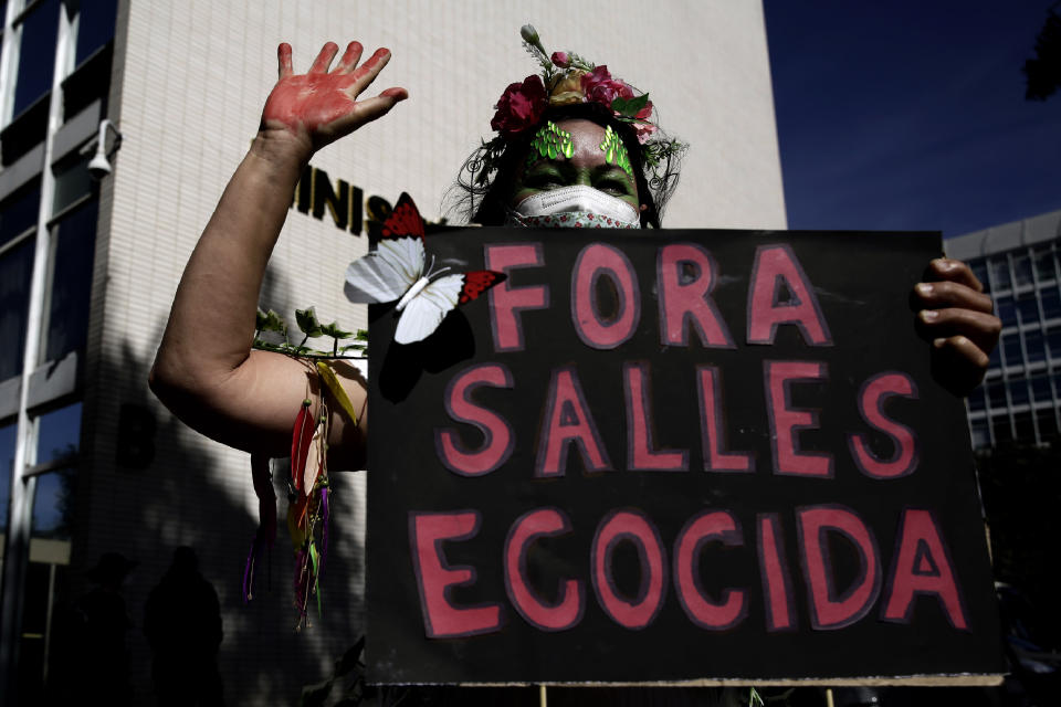 An activist holds a poster with a message that reads in Portuguese: "Out Salles Ecocida" directed at the Environment Minister Ricardo Salles, during a protest against the government's environmental policies, marking World Environment Day, in Brasilia, Brazil, Saturday, June 5, 2021. (AP Photo/Eraldo Peres)